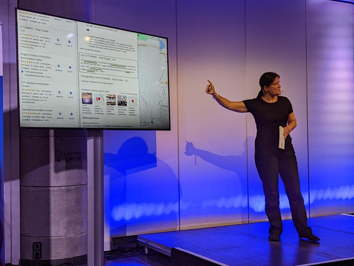 Frau auf der Bühne vor einem Monitor mit einer Slide mit beispielhaften Google Business Profil